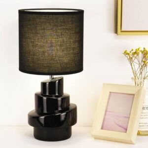 Black sculptural ceramic table lamp with a textured black shade styled in a cozy modern minimalist bedroom with moody ambient lighting
